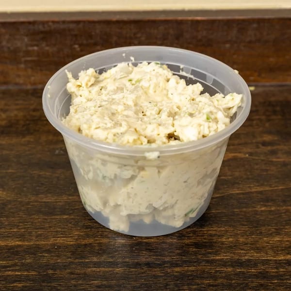 A clear plastic container filled with creamy chicken salad, sitting on a dark wooden table.