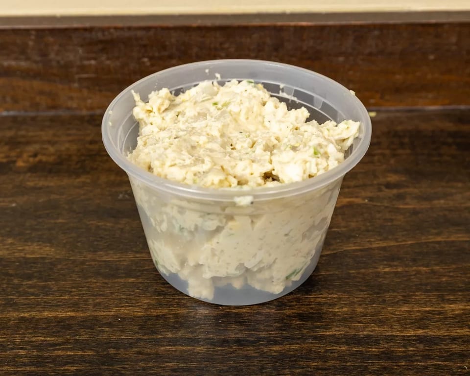 A clear plastic container filled with creamy chicken salad, sitting on a dark wooden table.