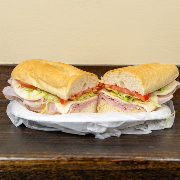 A large deli sub sandwich, cut in half, filled with ham, cheese, lettuce, and tomato.