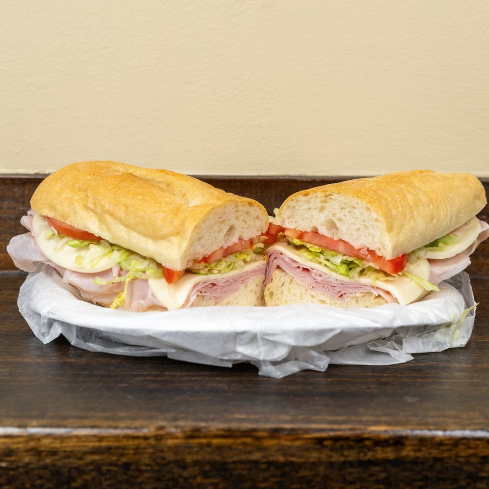 A large deli sub sandwich, cut in half, filled with ham, cheese, lettuce, and tomato.