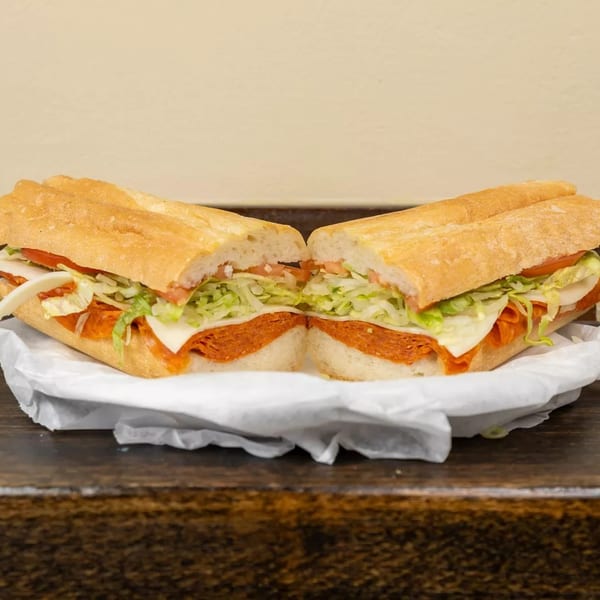 A large Italian sub sandwich, cut in half, filled with pepperoni, cheese, lettuce, and tomato.