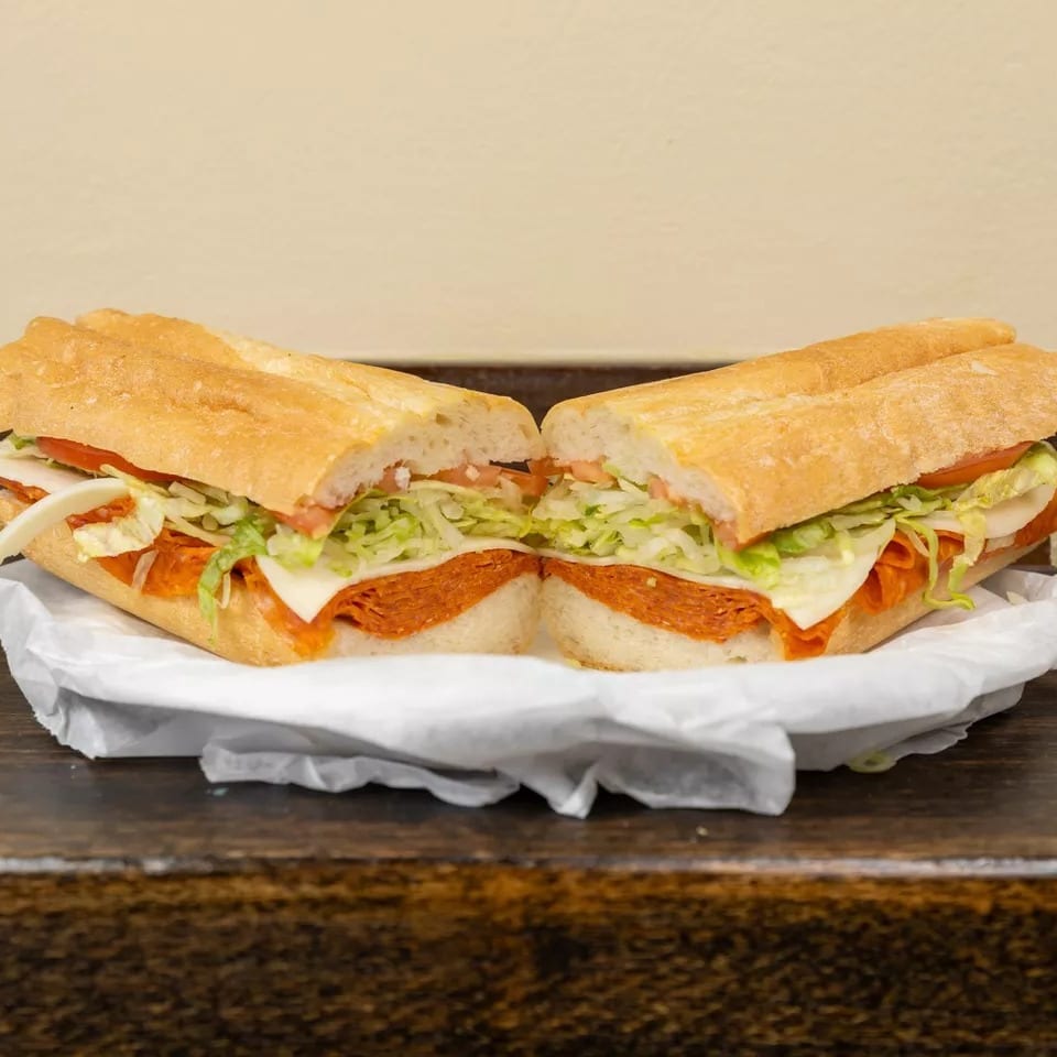 A large Italian sub sandwich, cut in half, filled with pepperoni, cheese, lettuce, and tomato.