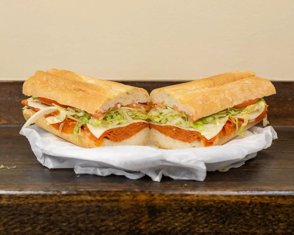 A large Italian sub sandwich, cut in half, filled with pepperoni, cheese, lettuce, and tomato.