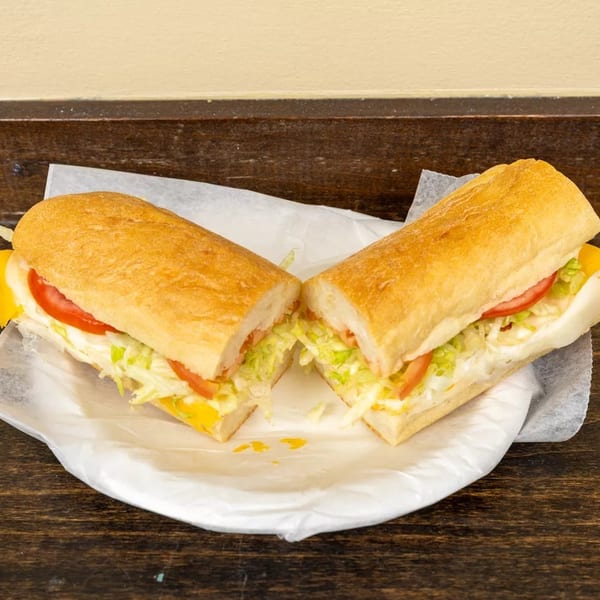 A submarine sandwich, cut in half, with lettuce, tomato, and cheese on a white paper plate.
