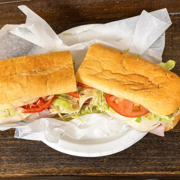 A large deli sub sandwich, cut in half, with lettuce, tomato, and meat on a paper plate.