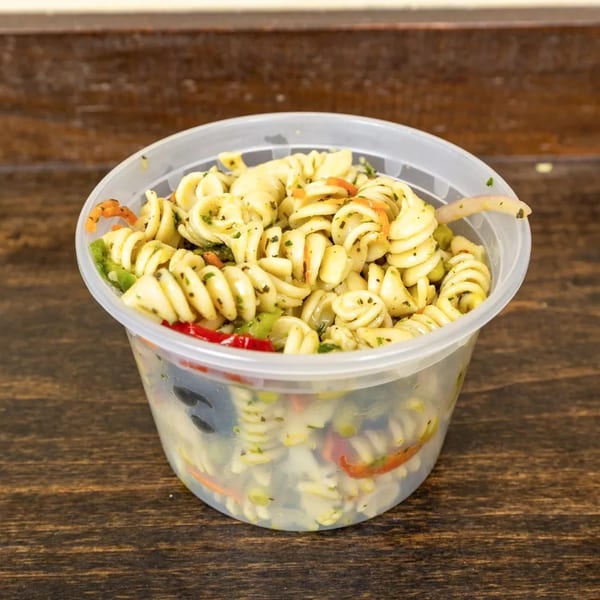 A clear plastic container filled with pasta salad, featuring rotini, vegetables, and herbs.