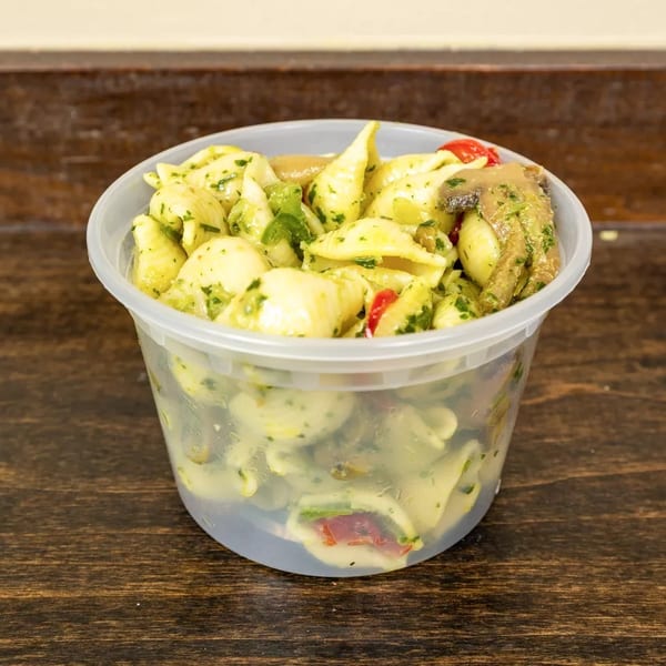 Pasta salad with pesto, mushrooms, and red peppers in a clear plastic container.