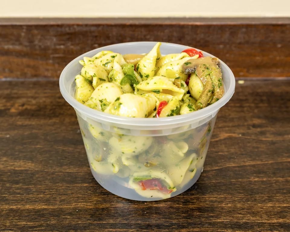 Pasta salad with pesto, mushrooms, and red peppers in a clear plastic container.