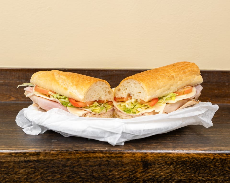 A large sub sandwich, cut in half, filled with meat, cheese, lettuce, and tomato.