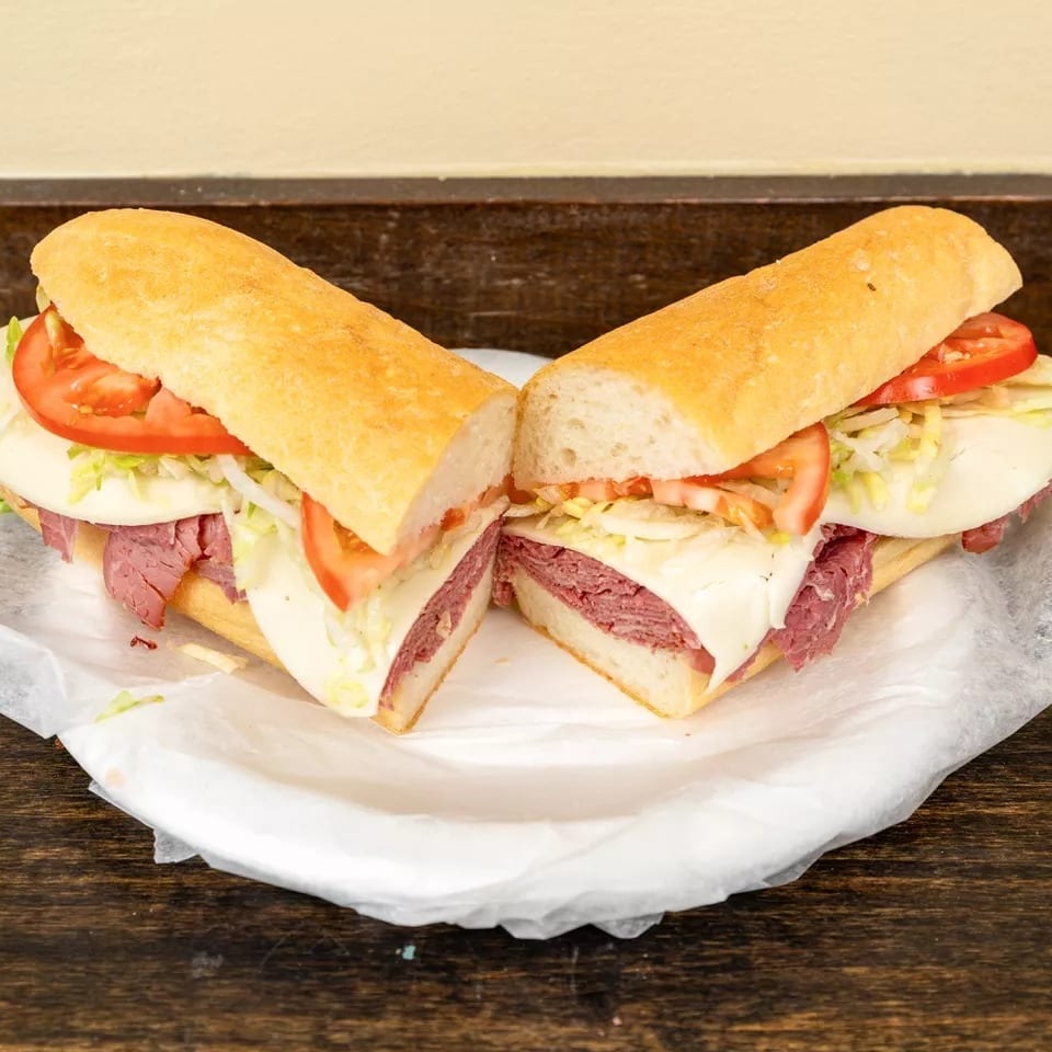 A large deli sandwich, cut in half, filled with meat, cheese, lettuce, and tomatoes on a white paper.