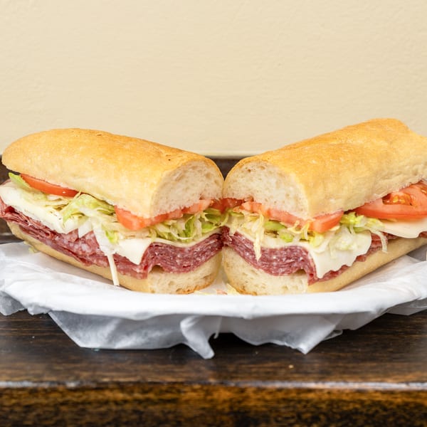A large deli sub sandwich, cut in half, filled with salami, cheese, lettuce, and tomato.