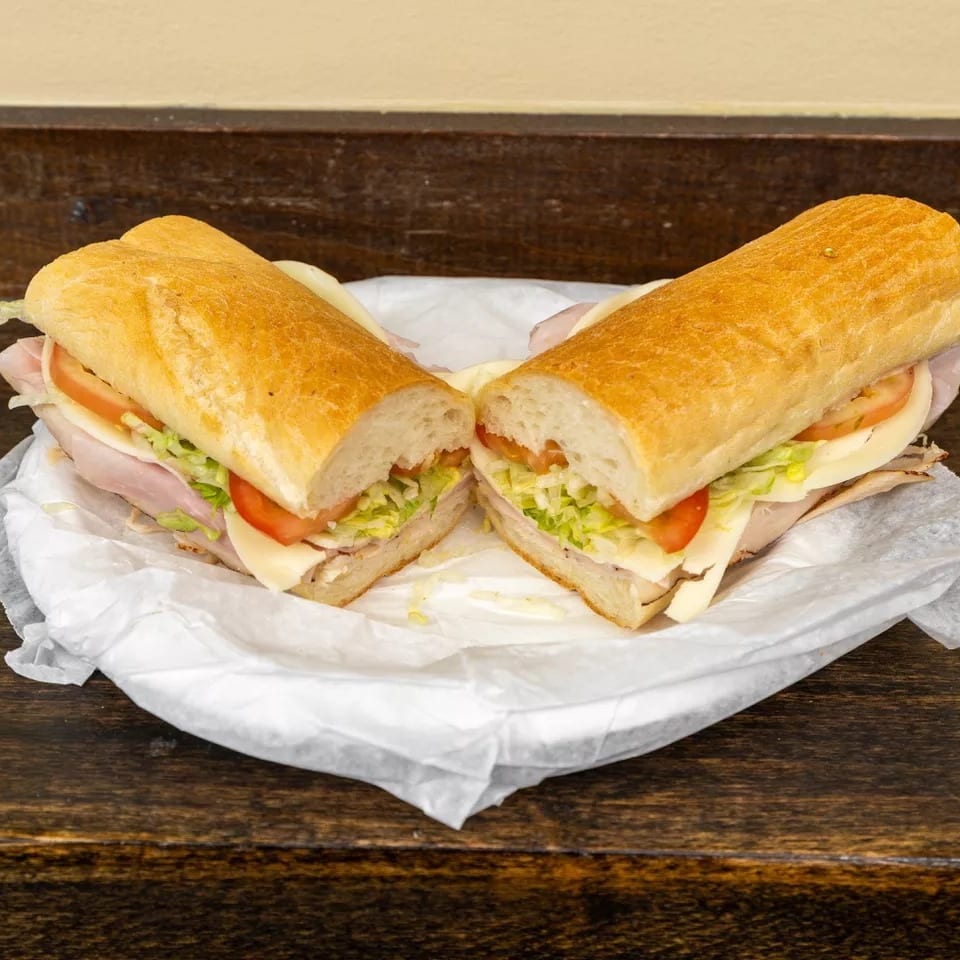 A large deli sub sandwich, cut in half, with turkey, cheese, lettuce, and tomato.
