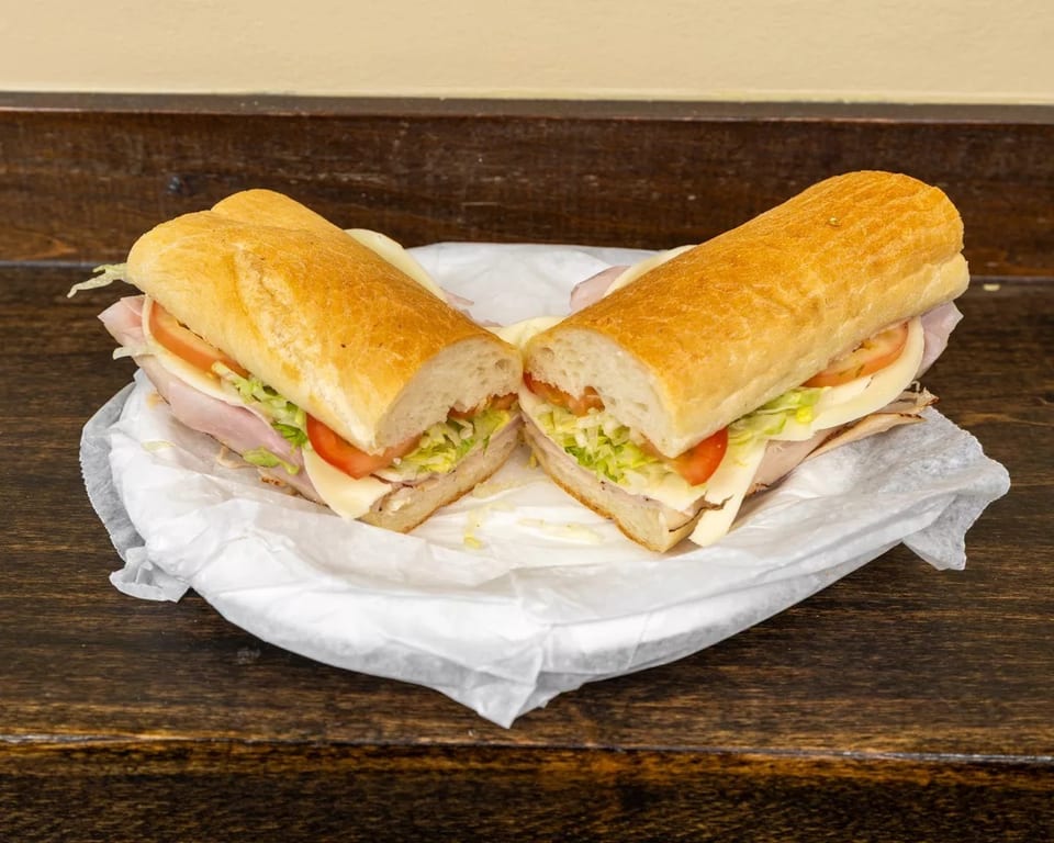 A large deli sub sandwich, cut in half, with turkey, cheese, lettuce, and tomato.